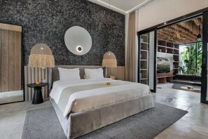 Relax in a spacious room with a large bed, side tables, and a balcony offering a view of lush greenery.