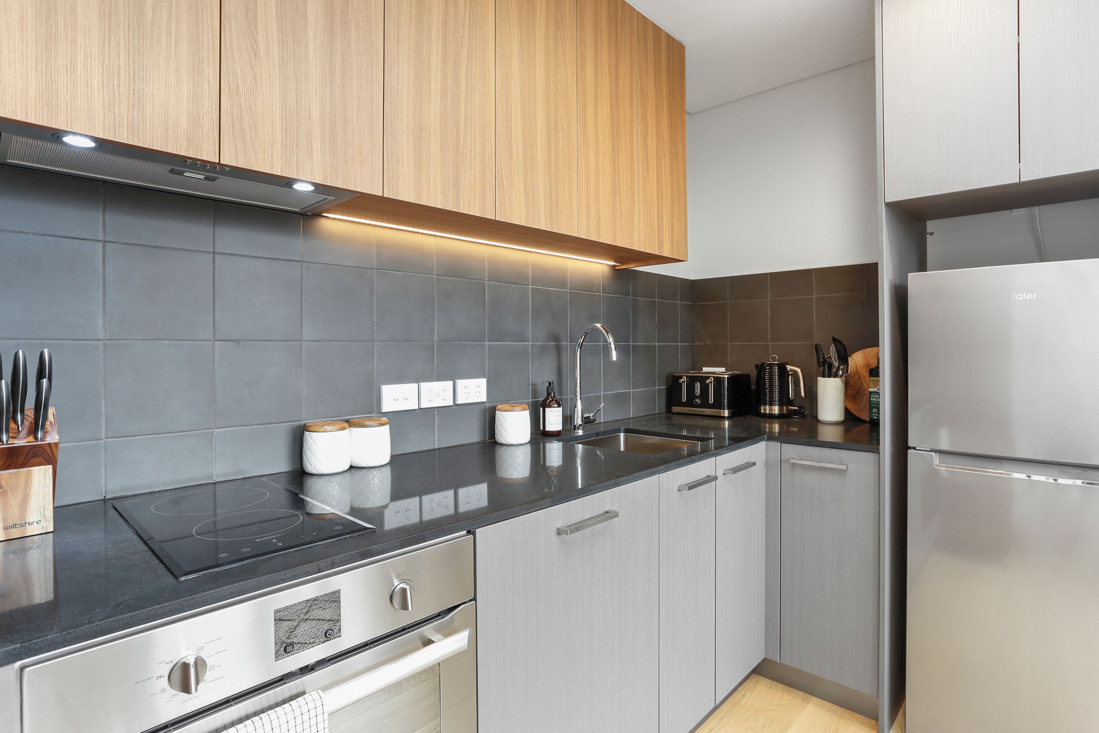 A modern kitchen with grey cabinets, a black countertop, and stainless steel appliances.