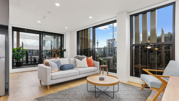 Una sala de estar moderna con un sofá, una mesa de centro y vistas a la ciudad a través de amplios ventanales.