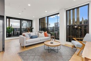 A modern living room with a sofa, coffee table, and a view of the city through large windows. - Lighthouse Apartments by Urban Rest (Auckland)