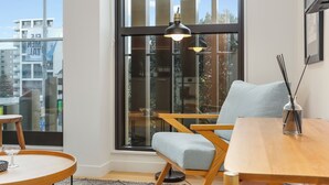 Una sala moderna con un gran ventanal, una mesa de comedor de madera, un sillón azul claro y una mesita auxiliar con un vaso.