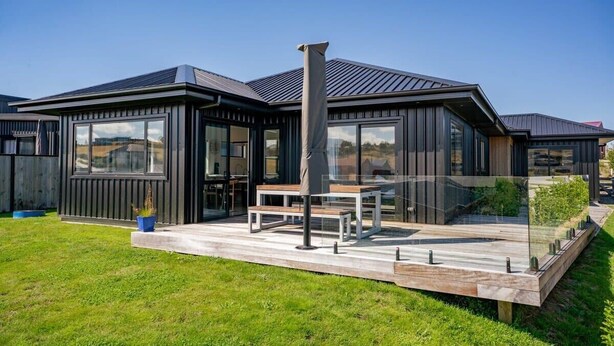 A modern house with a large deck, a chimney, and a clear sky. - Views on Farrant Summ (Wānaka)