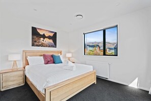 Un dormitorio con una cama de madera, dos mesitas de noche, un ventanal con vistas y un cuadro en la pared.