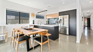 A modern kitchen with a central island, stainless steel appliances, and a dining area with wooden chairs and a table. - Views on Farrant Summ (Wānaka)