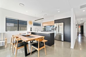 Une cuisine moderne dotée d’un îlot central, d’appareils électroménagers en acier inoxydable et d’un coin repas avec des chaises et une table en bois.