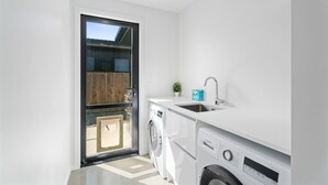 A compact kitchen with a washing machine, a sink, and a window. - Views on Farrant Summ (Wānaka)