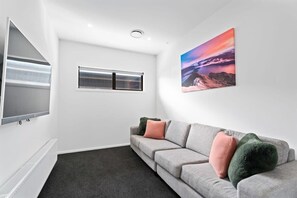 A modern living room with a grey sofa, a flat-screen TV, a window, and a painting on the wall. - Views on Farrant Summ (Wānaka)