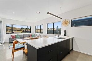 Une cuisine moderne dotée d’un grand îlot central, d’un coin repas avec un canapé et de grandes fenêtres offrant une vue sur la campagne.