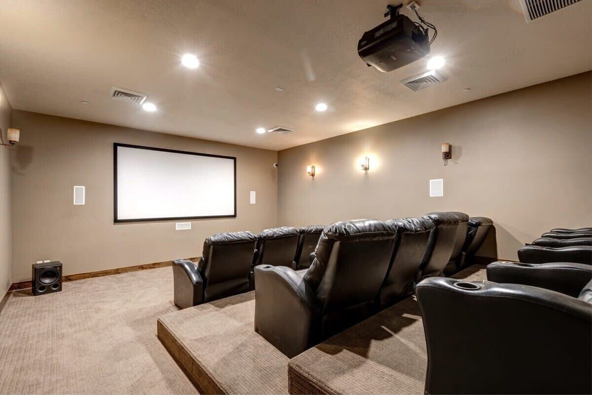 A home theater room with a large screen, leather reclining chairs, carpeted floor, and a projector.