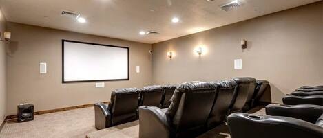 A home theater room with a large screen, leather reclining chairs, carpeted floor, and a projector.