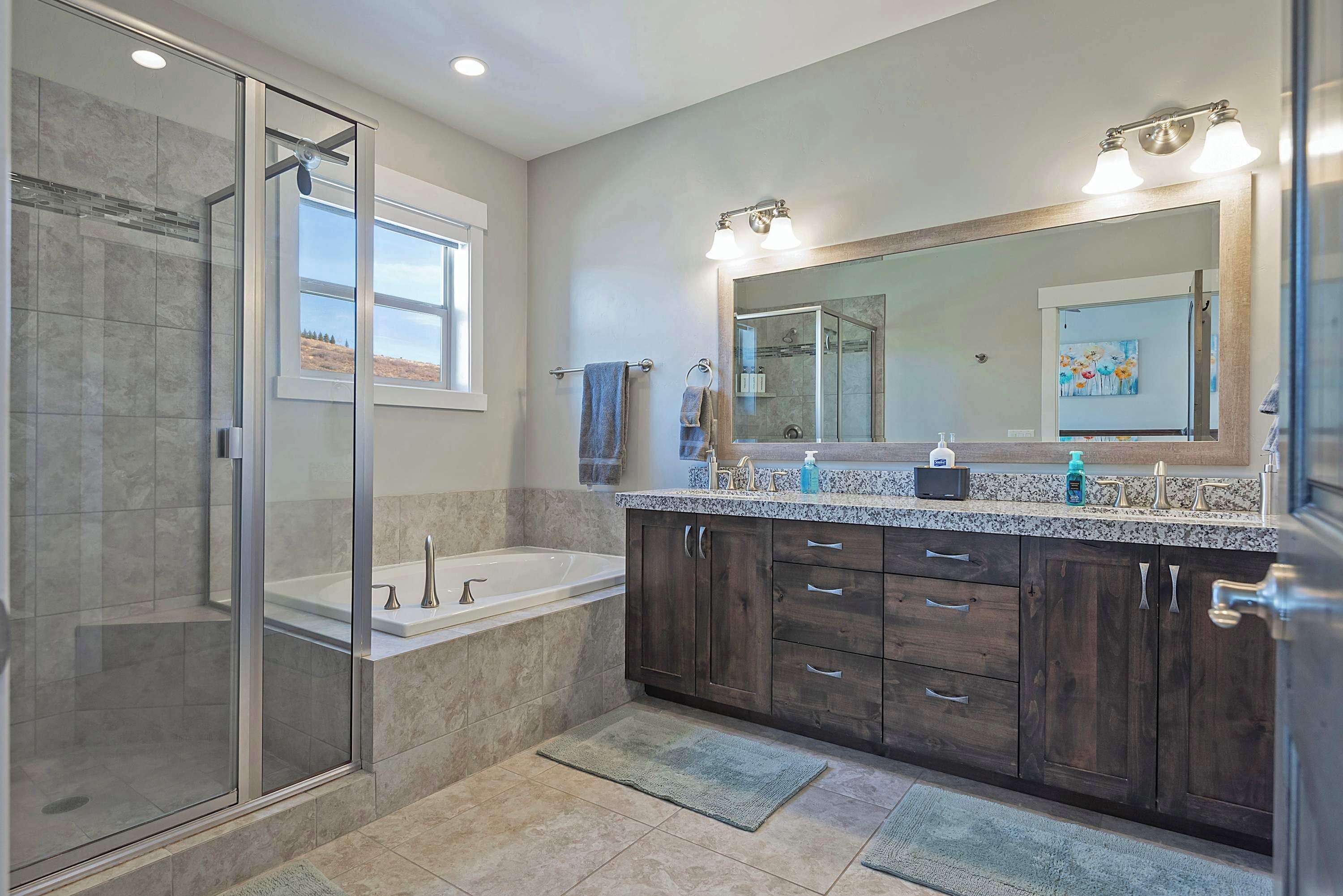 A modern bathroom with a glass-enclosed shower, a bathtub, and a vanity with a large mirror and dual sinks.