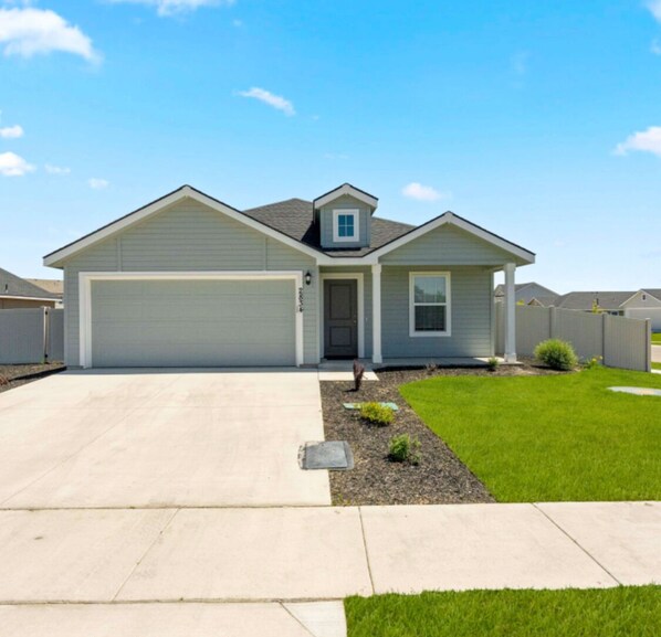 A single-story house with a garage, a front door, and a small front yard with grass and a flower bed.