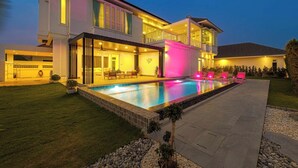 A modern two-story house with a swimming pool, outdoor seating, and a well-lit patio area. - Luxury 4 Bedroom Pool Villa - PV8 (Hua Hin)
