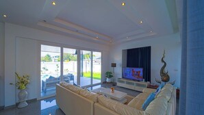 A modern living room with a large sofa, a flat-screen TV, and a decorative wall piece. - Luxury 4 Bedroom Pool Villa - PV8 (Hua Hin)