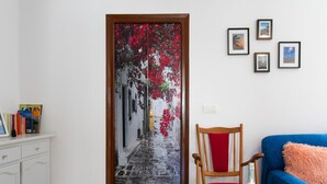 A room with a door decorated with a red floral pattern, a wooden chair with a red cushion, a blue sofa with a fluffy pillow, and a small table with a bottle and glass. - Apartment Parra by Interhome (Nerja)