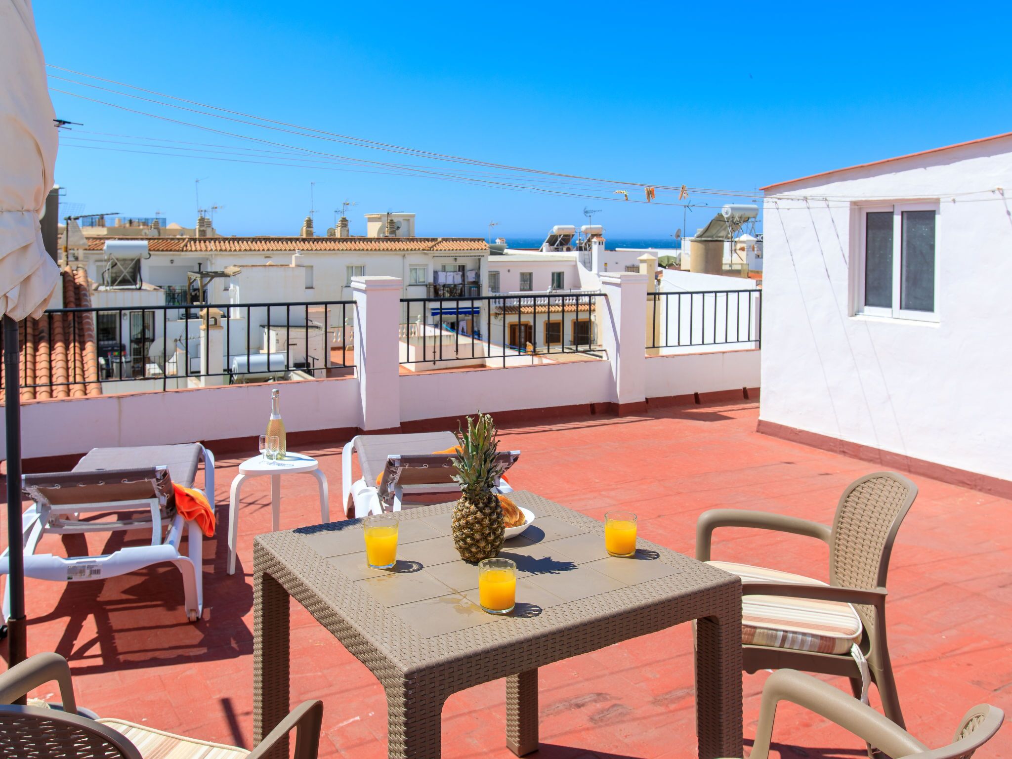Une terrasse sur le toit avec une table dressée pour deux personnes, agrémentée d’un ananas et de deux verres de jus d’orange.