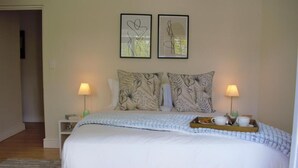 Un dormitorio ordenado con una cama grande, dos mesitas de noche con lámparas y una bandeja con tazas y una vela sobre la cama.