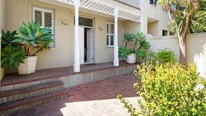 Una casa de dos pisos con un balcón, plantas en macetas y un camino de ladrillos que lleva a la entrada.