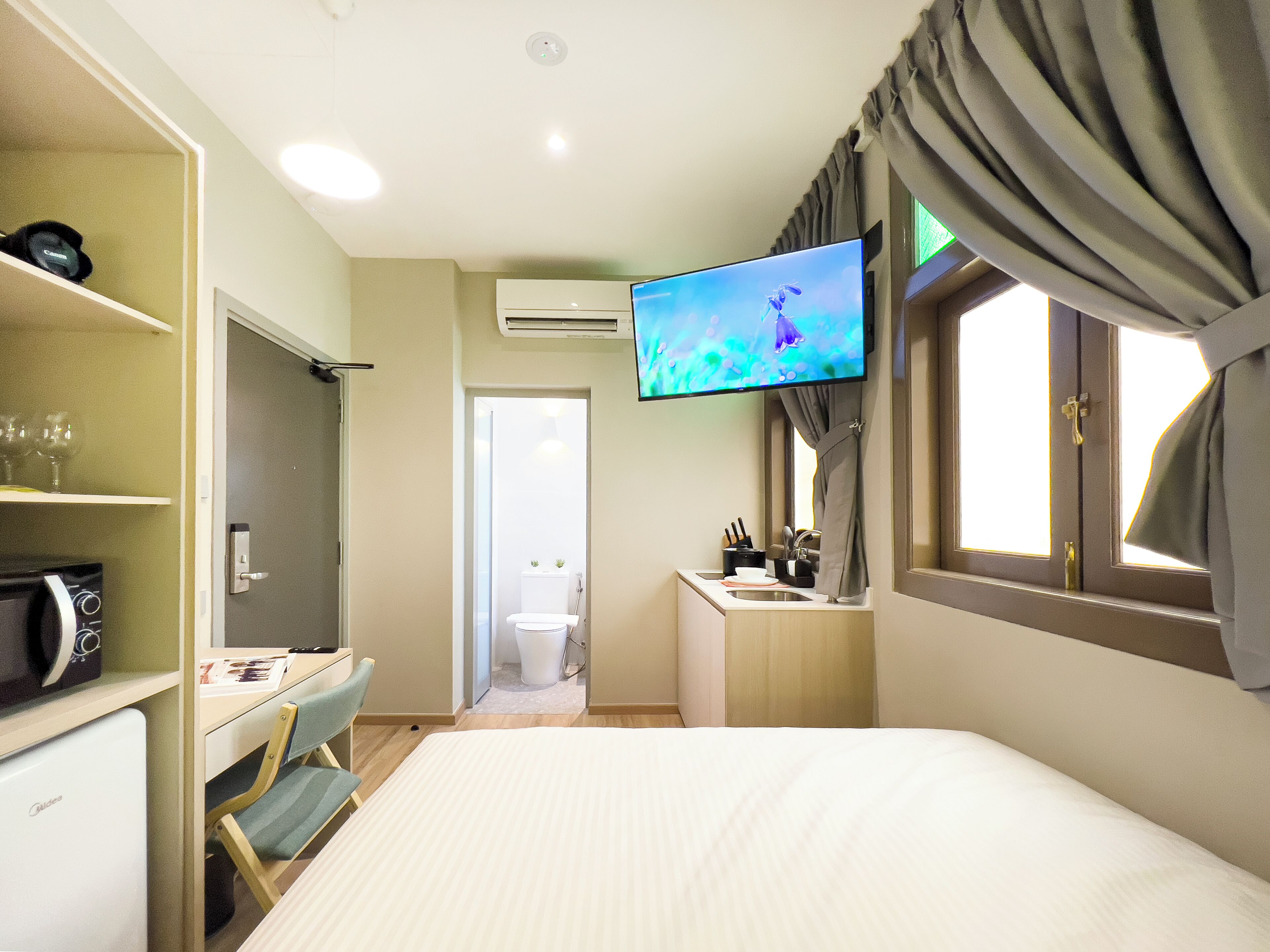 A hotel room with a bed, a desk with a chair, a wardrobe, a bathroom, and a TV mounted on the wall.