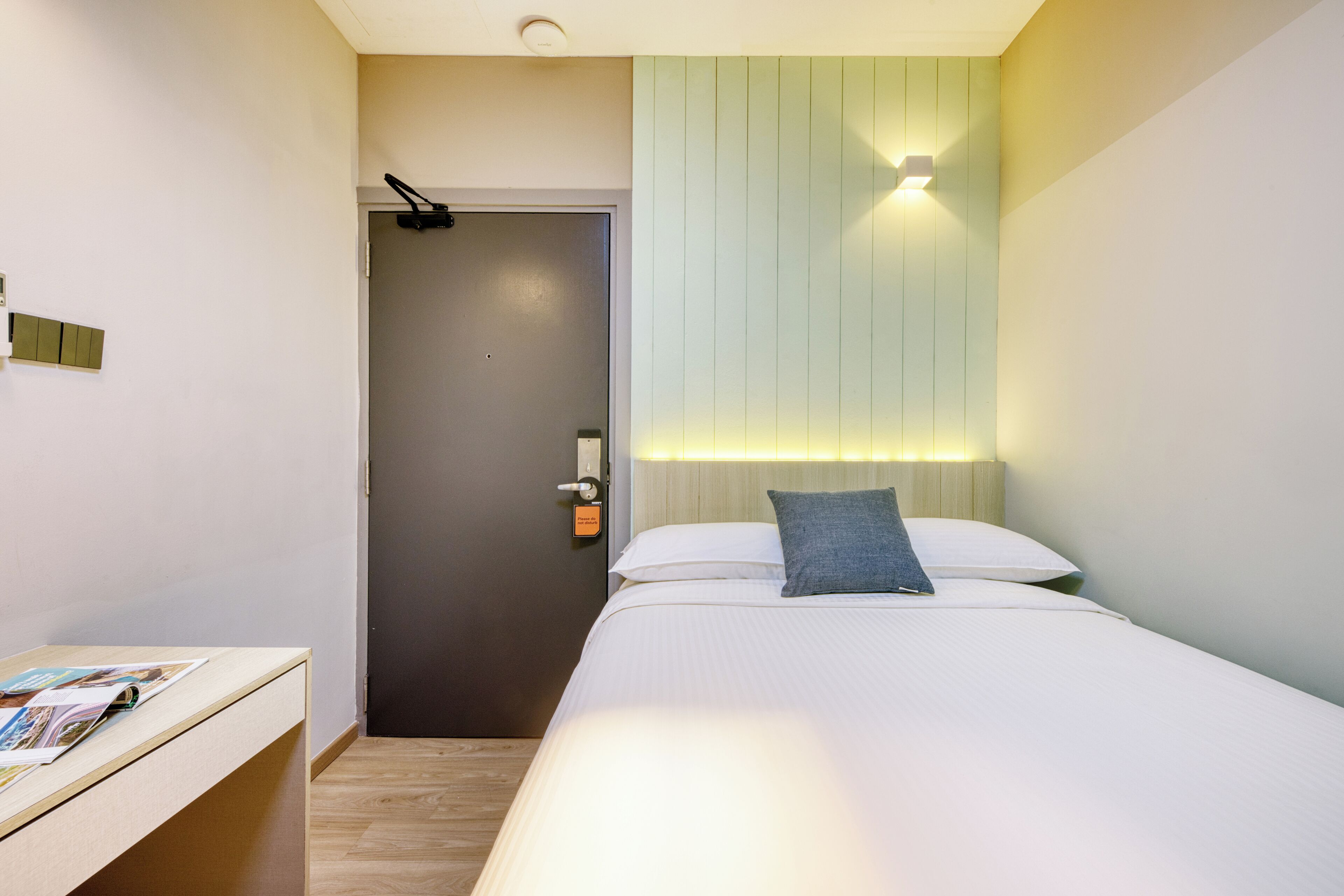 Ett modernt hotellrum med en säng, ett nattduksbord och en dörr som leder till ett annat rum.