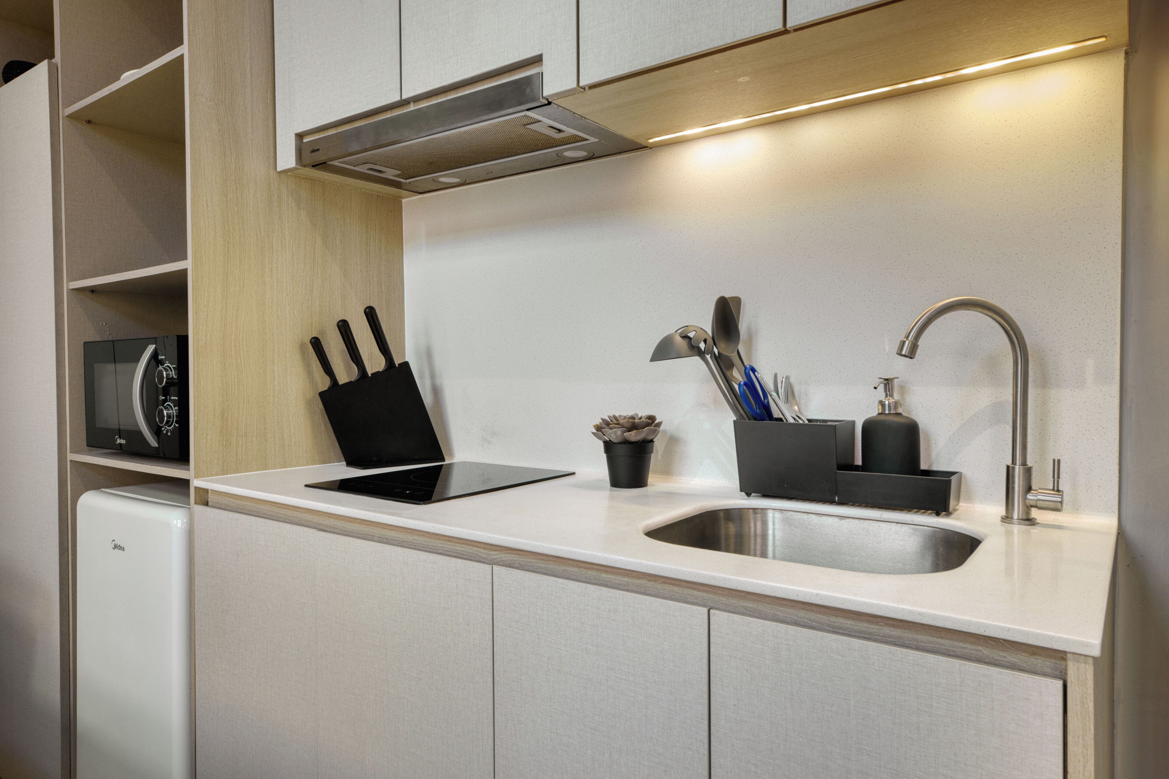 Una cocina moderna con lavavajillas integrado, un lavamanos de acero inoxidable y una campana extractora.