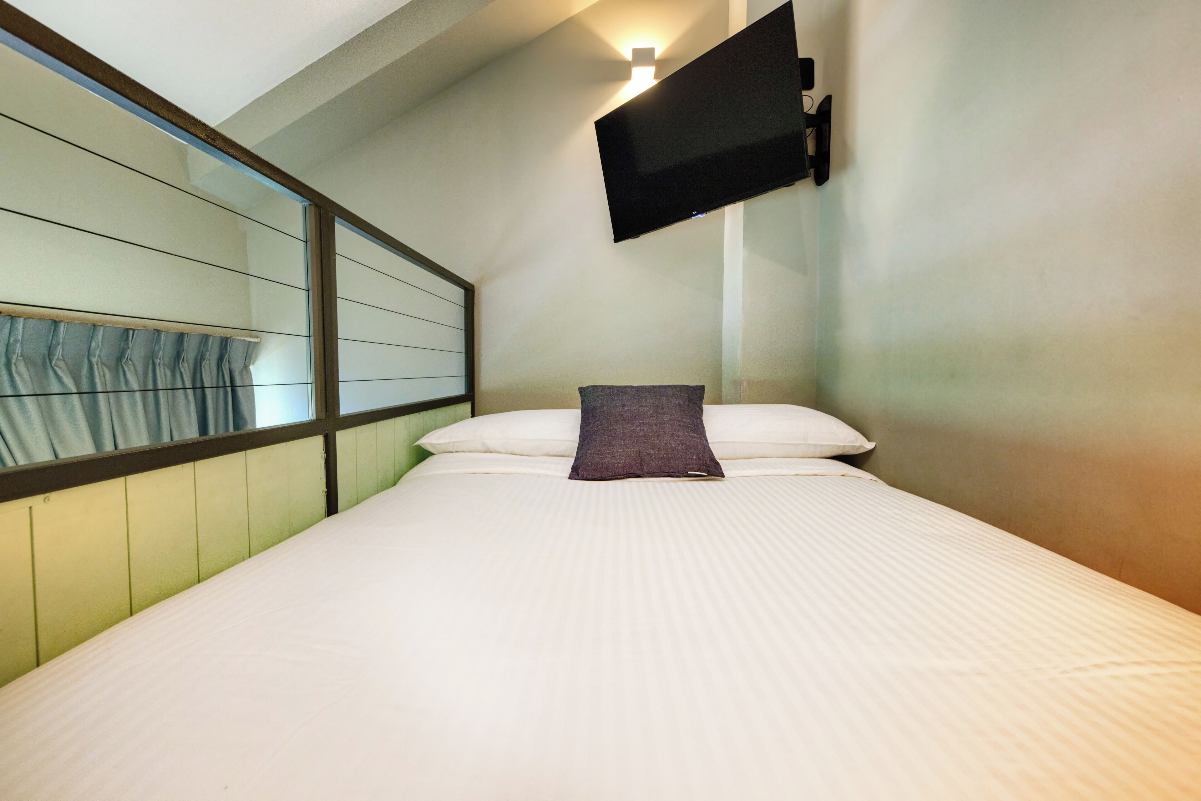 Quarto de hotel com cama, televisão montada e janela com cortinas.