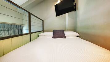 Quarto de hotel com cama, televisão montada e janela com cortinas.