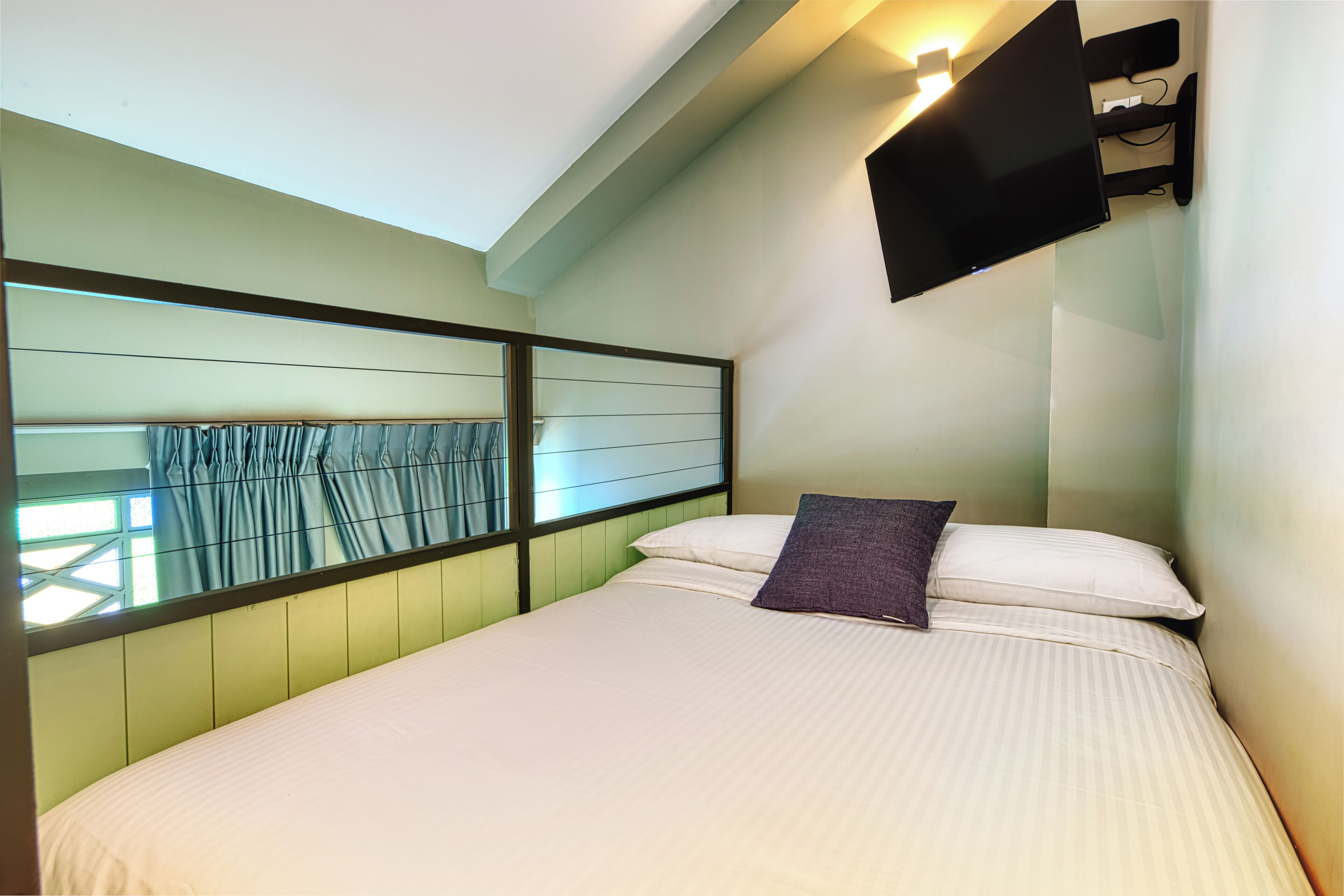 Un dormitorio con cama, ventana con cortinas, televisor montado y estante en la pared.