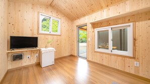 A room with wooden walls, a flat-screen TV, a washing machine, and two windows.