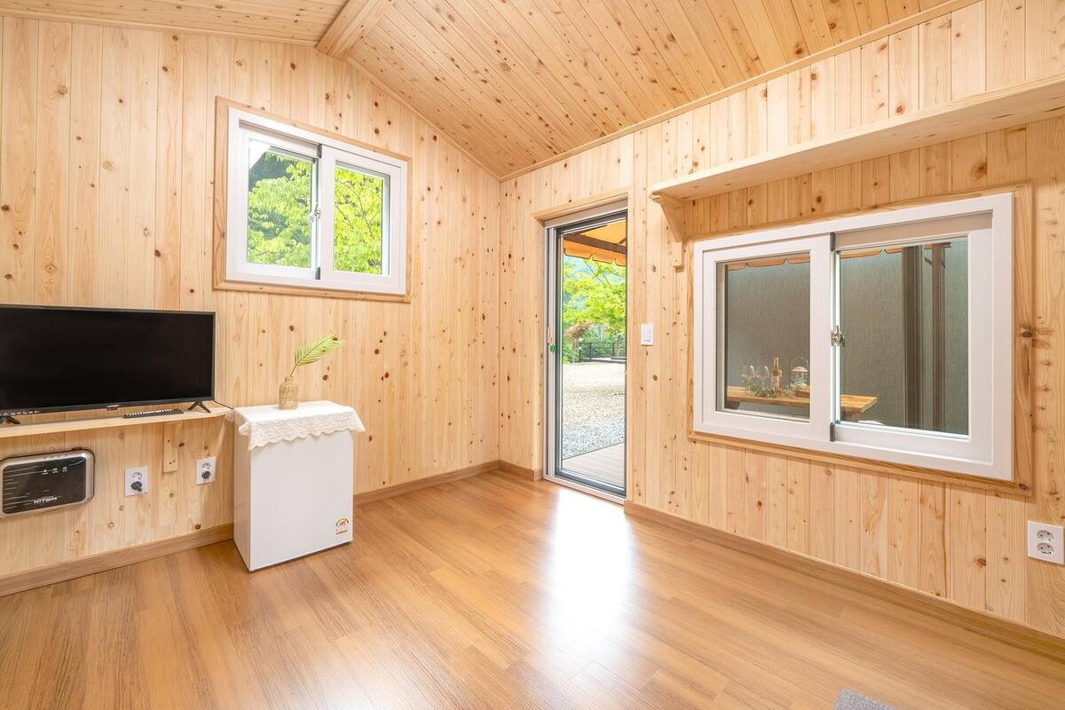 A room with wooden walls, a flat-screen TV, a washing machine, and two windows.