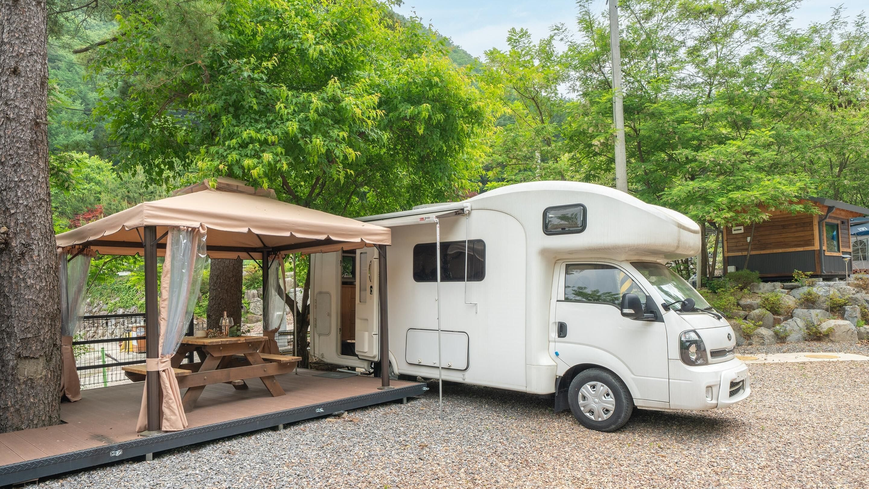Een witte camper met een afgedekte picknicktafel en een klein terras.