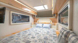A cozy RV bedroom with a bed, two pillows, a window, and a ceiling light.