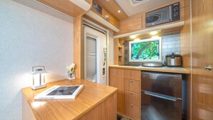 A compact kitchenette with a built-in oven, a coffee maker, and a television displaying a nature scene.