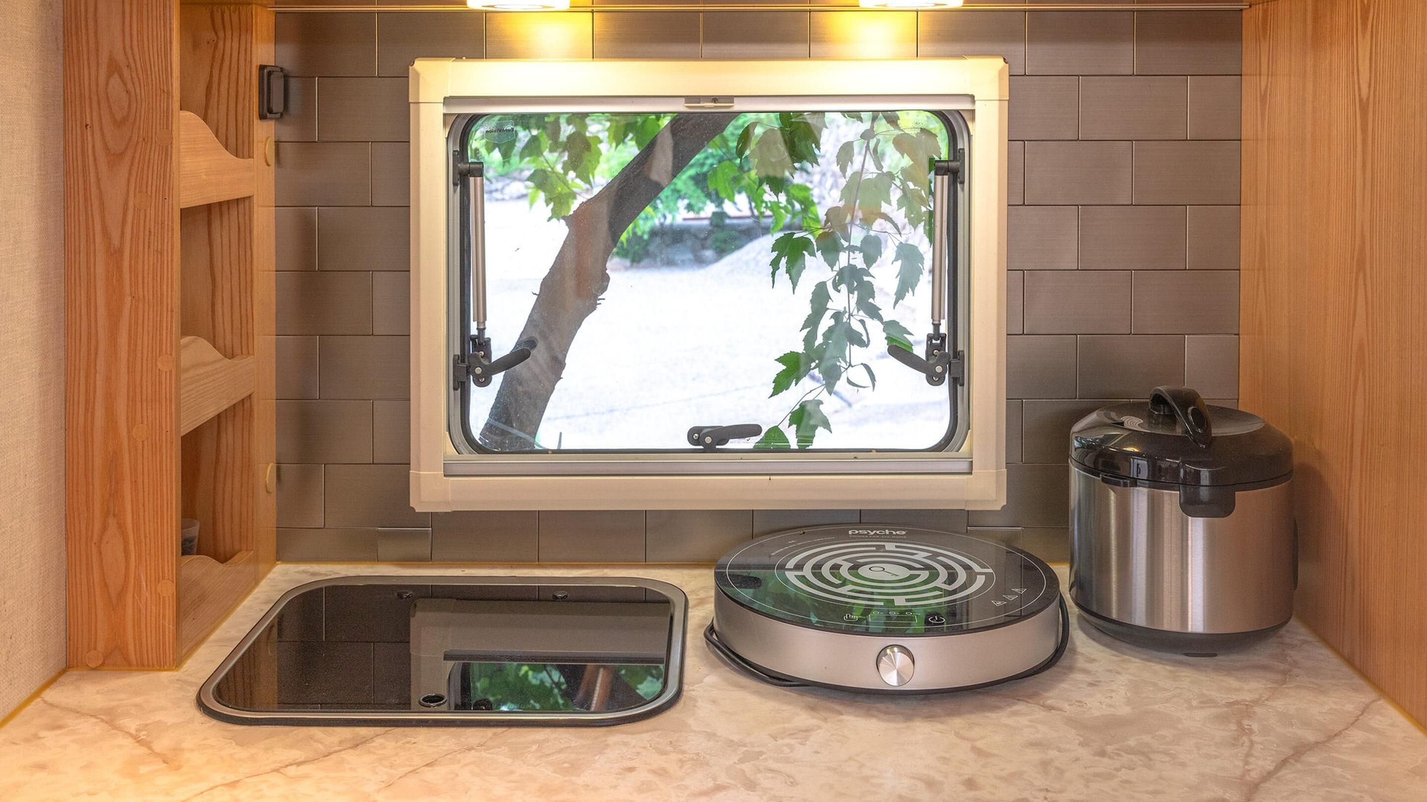A compact kitchen with a window, a built-in rice cooker, and a compact microwave.