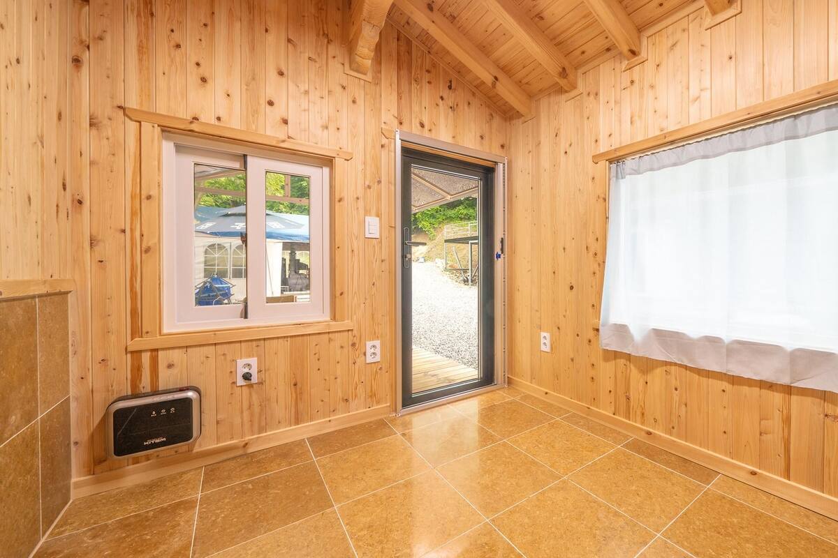 A wooden interior with a tiled floor, a door leading outside, and a window with a view of the outside.