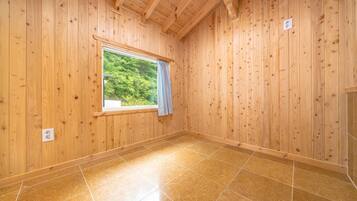 A room with wooden walls, a window with a curtain, and a tiled floor.
