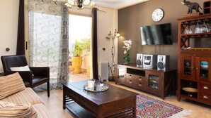 Un salon comprenant un canapé, une table basse, un téléviseur, une horloge et un meuble contenant de la verrerie.