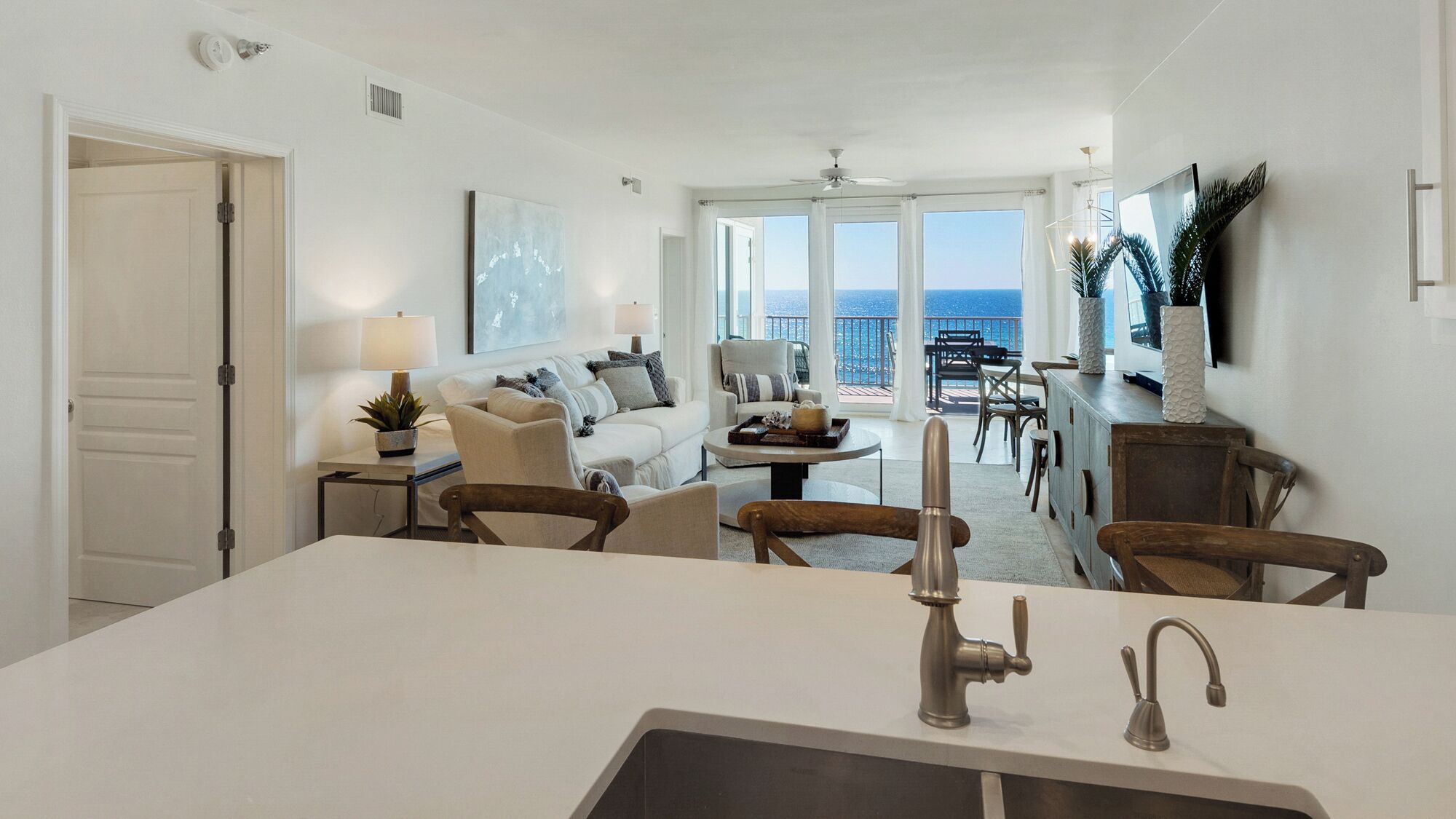 Une cuisine moderne dotée d’un îlot central, un coin repas offrant une vue sur la mer, et un salon avec un canapé et une table basse.