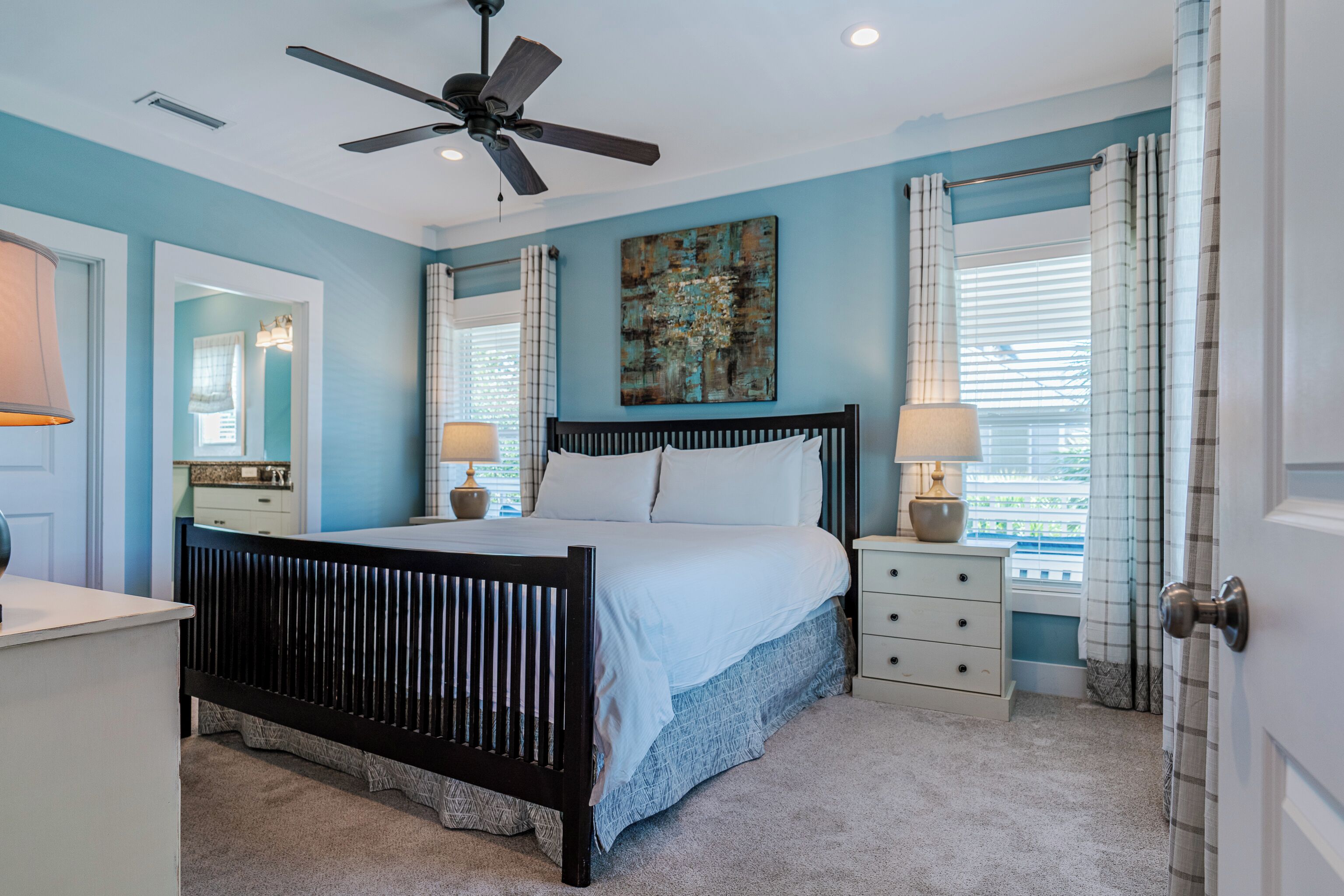 A bedroom with a bed, bedside tables, a ceiling fan, and a window with curtains.