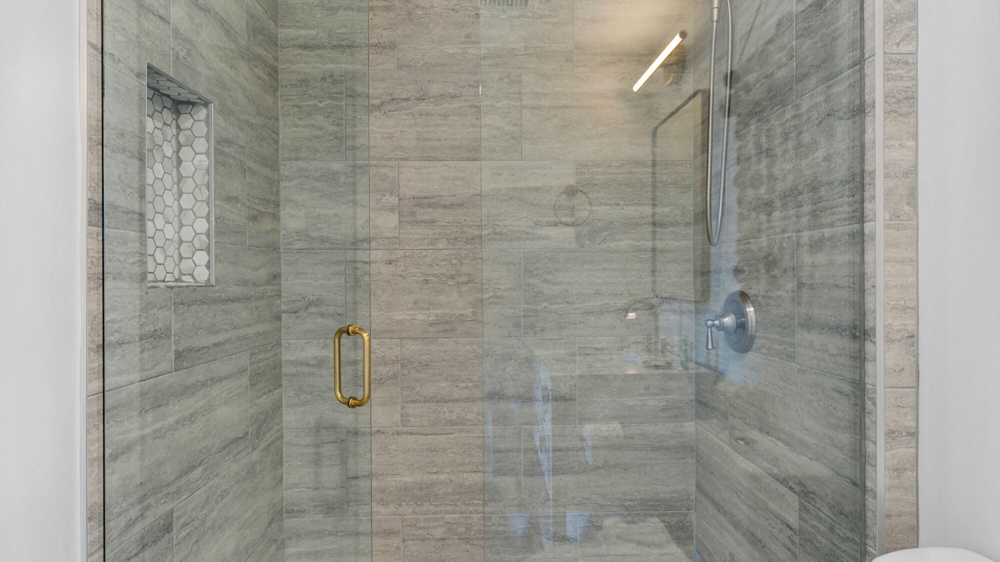 A glass-enclosed shower with a marble wall, a hexagonal tile pattern on the left, and a showerhead on the right.