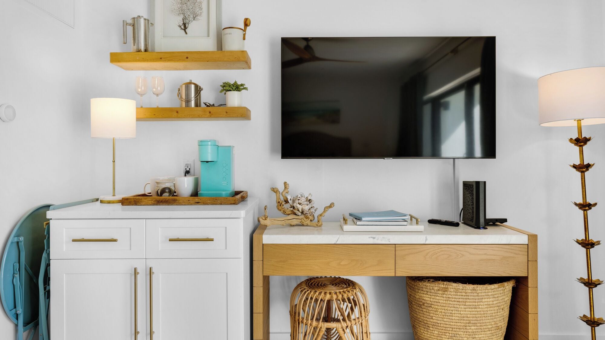 A modern living room with a wooden desk, a mounted TV, and a coffee machine.
