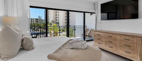 A modern hotel room with a large bed, a wooden dresser, a flat-screen TV, and a balcony with a view of the city.