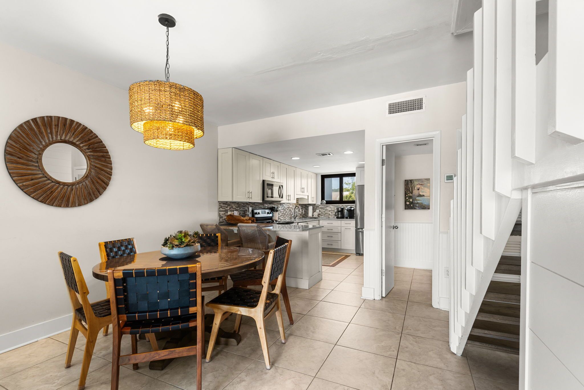 A modern kitchen with white cabinets, a central island, and a dining area with a wooden table and chairs.