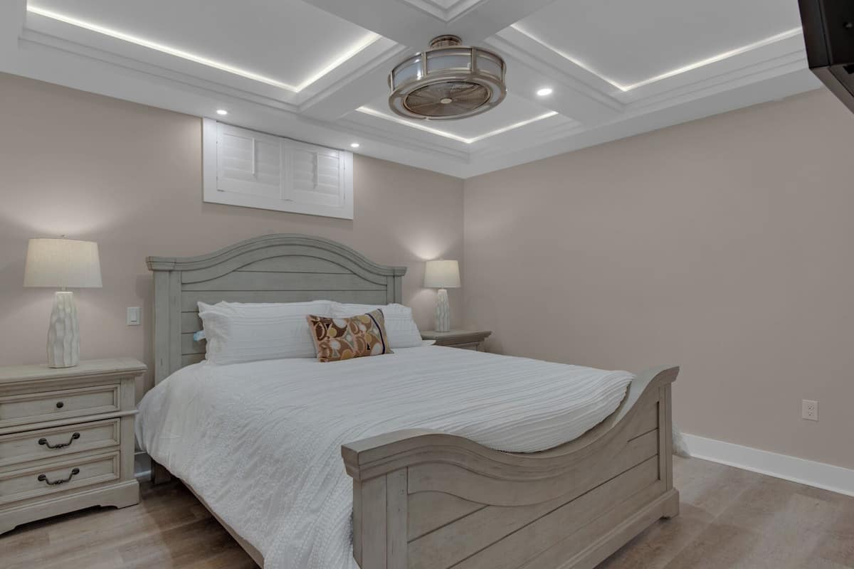 A bedroom with a bed, nightstands, a ceiling fan, recessed lighting, and a wall-mounted artwork.
