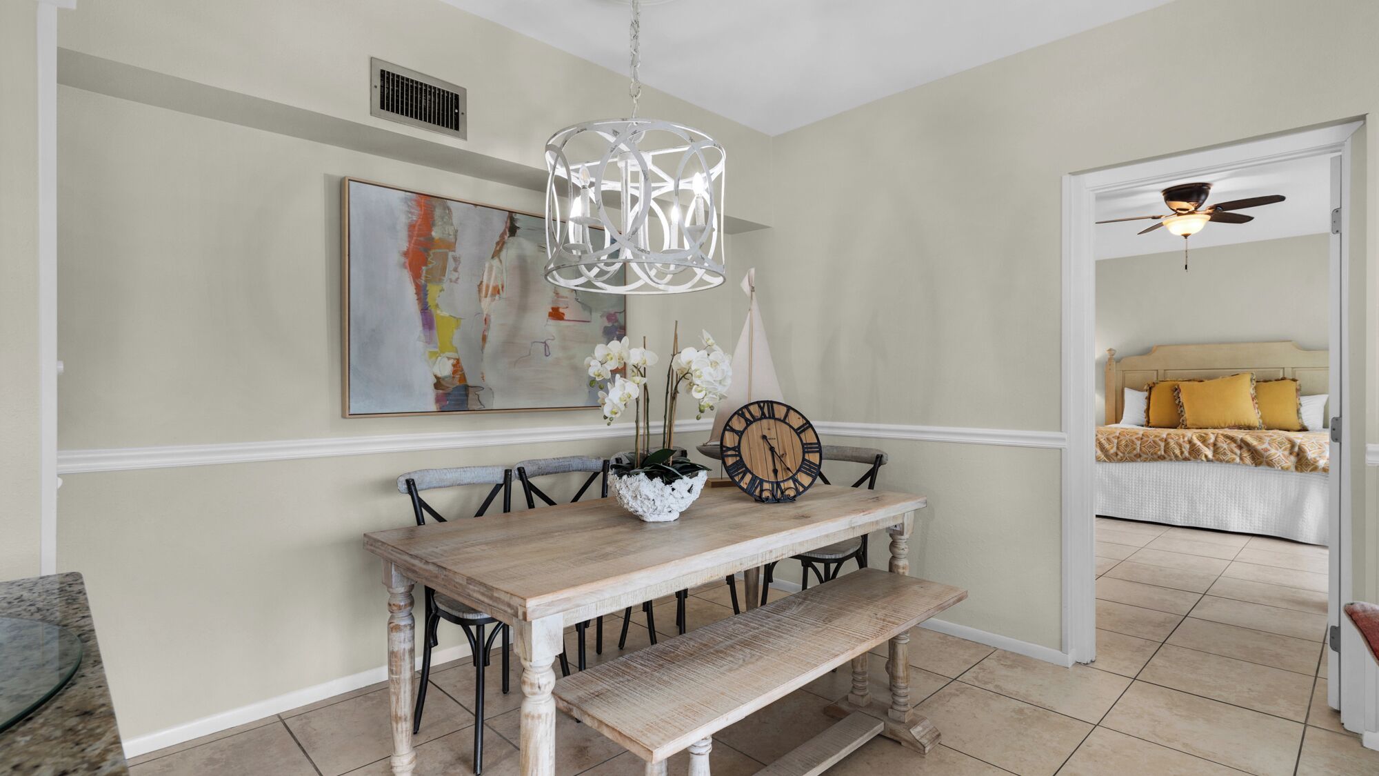 A dining area with a wooden table, bench, and decorative items including a clock and flowers.