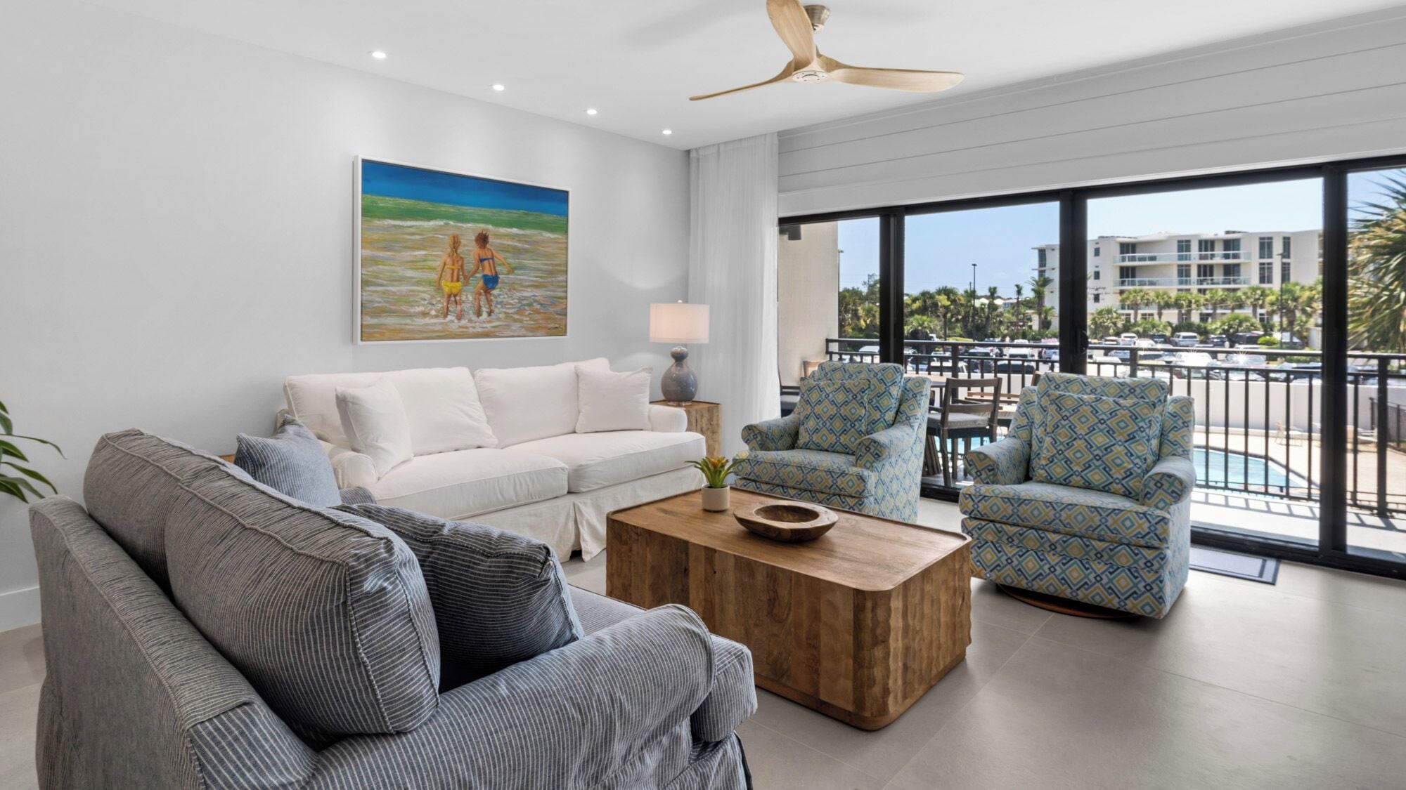 A modern living room with a white sofa, striped armchairs, a wooden coffee table, and a painting of a beach scene.