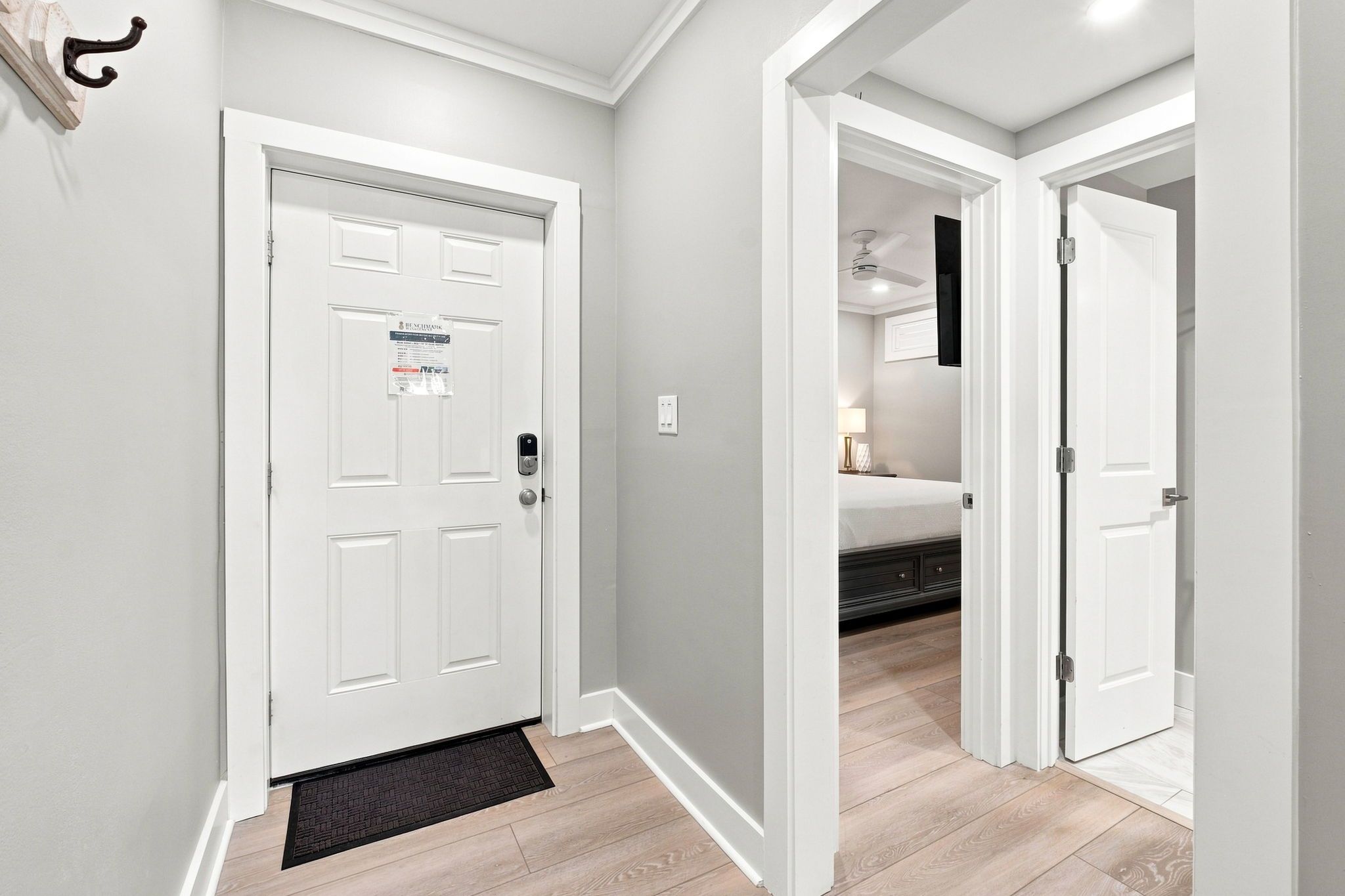 A hallway with a white door, a doormat, and a bed in the adjacent room.