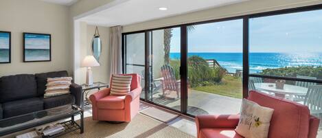 A spacious living room with a large sliding glass door leading to a balcony overlooking the ocean.