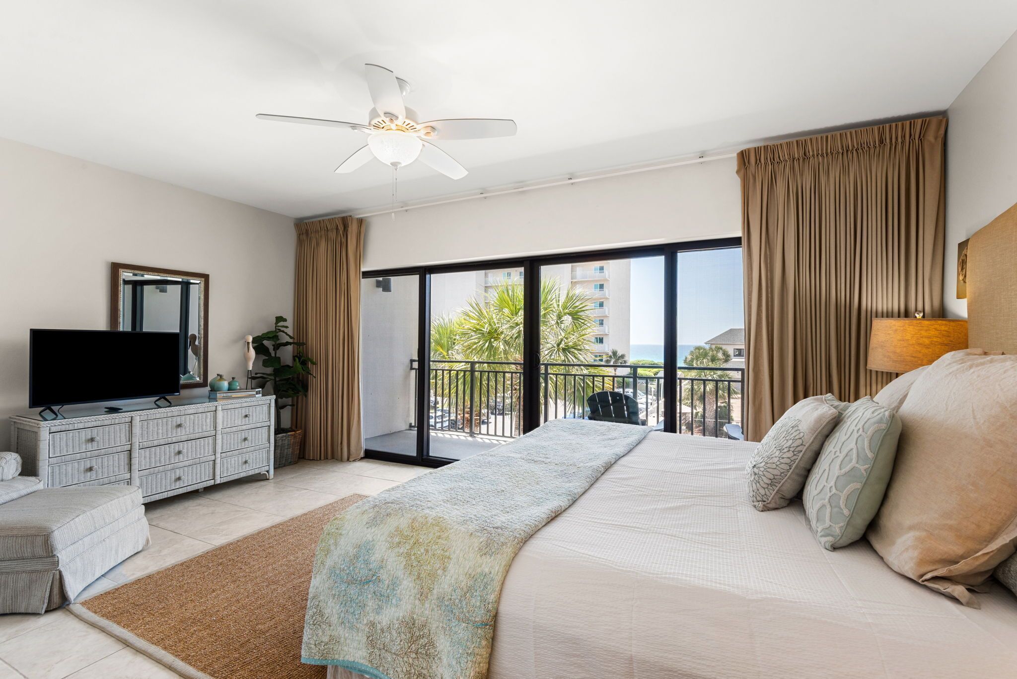 Ein Schlafzimmer mit Bett, Fernseher, Schminktisch, einem Balkon mit Blick und Deckenventilator.