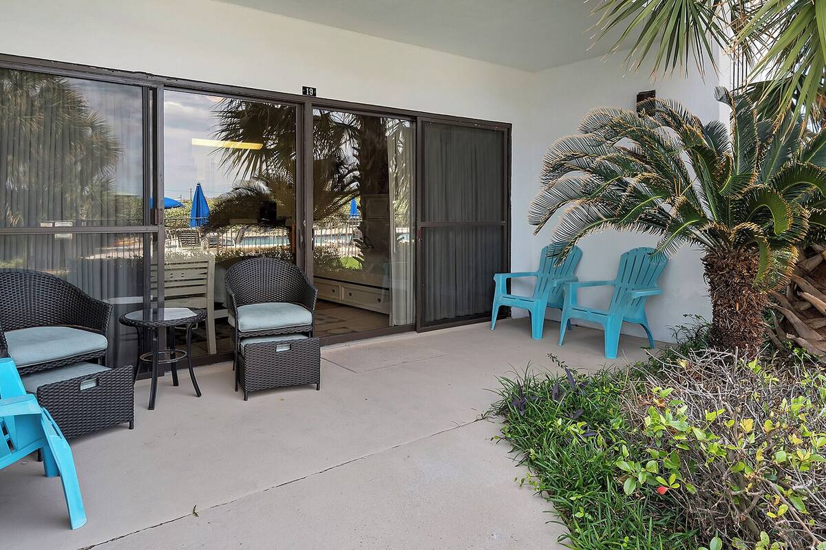 A covered outdoor seating area with wicker furniture and a palm tree.